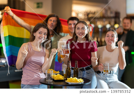 Sports fans with LGBT flag celebrate their favorite team victory in beer pub 139785352