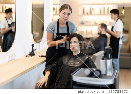Young female hairdresser giving haircut to adult woman Young female hairdresser giving haircut to adult woman 139785372