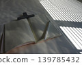 A desk with a grid notebook and pen, where light and shadow fall through the blinds. 139785432