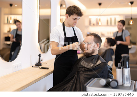 Young guy hairdresser giving haircut to young man 139785440