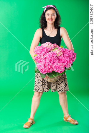 Portrait of positive adult woman with basket of pink flowers on green background. Chroma key compositing 139785467