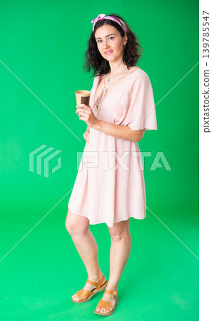 Woman in pink dress drinking coffee against a green chroma key background. Chroma key compositing. 139785547