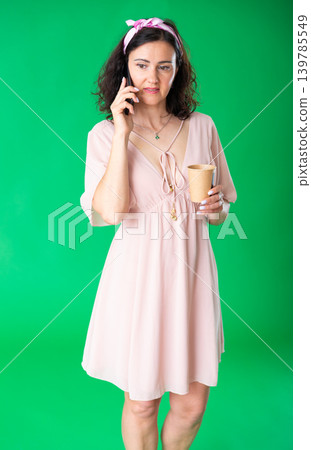Adult woman with a cup of coffee talking on the phone on green background. Chroma key compositing. 139785549