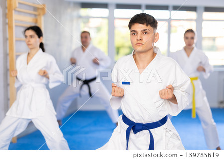 Middle-aged man attendee of karate classes practicing kata standing in row with others Middle-aged man attendee of karate classes practicing kata standing in row with others 139785619