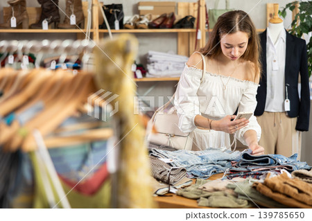 Attentive woman checking the quality of jeans or shorts using a steamer QR code on label 139785650