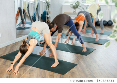Women and men practicing downward dog pose of yoga during fitness classes Women and men practicing downward dog pose of yoga during fitness classes 139785833