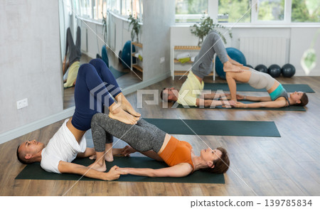 Lovers of active lifestyle perform pair yoga bridge and supported shoulderstand pose in gym Lovers of active lifestyle perform pair yoga bridge and supported shoulderstand pose in gym 139785834