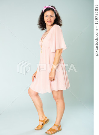 Portrait of cheerful adult woman in pink dress on gray background Portrait of cheerful adult woman in pink dress on gray background 139785853