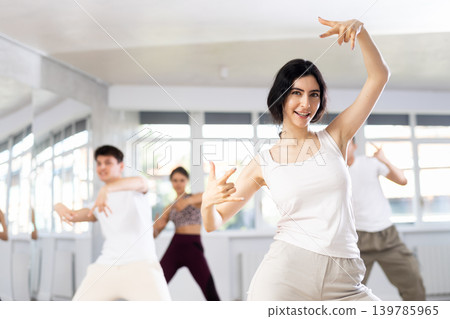 Happy emotional young female dancer rehearsing popping techniques during group workout in modern street dance studio Happy emotional young female dancer rehearsing popping techniques during group workout in modern street dance studio 139785965