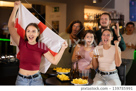 Company of fans of different ages waving flag of England and celebrating victory of favorite team in sports bar Company of fans of different ages waving flag of England and celebrating victory of favorite team in sports bar 139785991