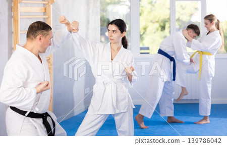 Young female attendee of karate classes fighting with middle-aged man in sports hall Young female attendee of karate classes fighting with middle-aged man in sports hall 139786042