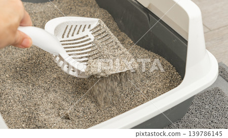 Hand holding a scoop removing cat litter from a gray plastic litter box with a textured mat underneath for easy cleaning Hand holding a scoop removing cat litter from a gray plastic litter box with a textured mat underneath for easy cleaning 139786145
