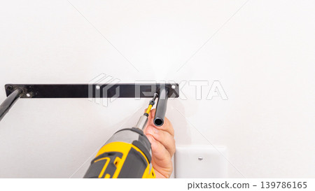 Mans hands aligning black metal shelf bracket on white wall during installation. Home improvement, bracket adjustment, DIY precise placement, mounting process. 139786165