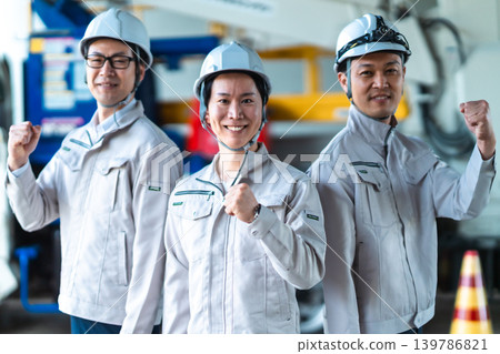 Three men in work clothes make a powerful victory pose in front of a special vehicle. Three men in work clothes make a powerful victory pose in front of a special vehicle. 139786821