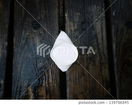一個被雨水打濕的白色紙杯卡在公園木製長椅的縫隙裡。 一個被雨水打濕的白色紙杯卡在公園木製長椅的縫隙裡。 139786845