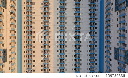 High-angle view of a modern high-rise residential apartment building with blue balconies and a swimming pool at the base during golden hour. 139786886