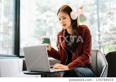young Asian freelancer works on her laptop in a modern cafe, representing remote work, digital nomad lifestyle, and professional success in a casual setting. young Asian freelancer works on her laptop in a modern cafe, representing remote work, digital nomad lifestyle, and professional success in a casual setting. 139786919