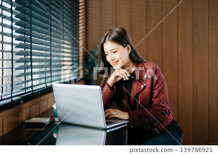 young Asian freelancer works on her laptop in a modern cafe, representing remote work, digital nomad lifestyle, and professional success in a casual setting. young Asian freelancer works on her laptop in a modern cafe, representing remote work, digital nomad lifestyle, and professional success in a casual setting. 139786921