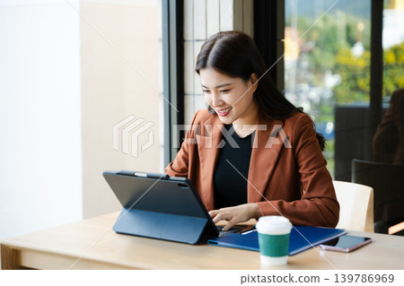 Asian businesswoman talking on smartphone while working on tablet at desk. Professional female multitasking with online communication 139786969