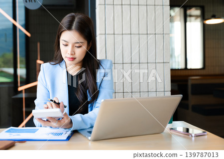 Asian businesswoman using smartphone and laptop in modern office. Professional female entrepreneur multitasking Asian businesswoman using smartphone and laptop in modern office. Professional female entrepreneur multitasking 139787013