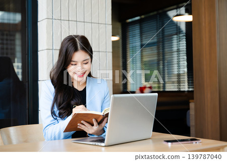 Asian businesswoman working online with laptop and notebook. Remote work, productivity, learning and freelance lifestyle concept in modern workspace Asian businesswoman working online with laptop and notebook. Remote work, productivity, learning and freelance lifestyle concept in modern workspace 139787040