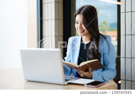 Asian businesswoman working online with laptop and notebook. Remote work, productivity, learning and freelance lifestyle concept in modern workspace 139787041