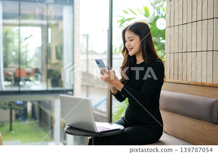 Asian businesswoman using laptop and smartphone while reviewing documents in a modern workspace, symbolizing productivity, remote work Asian businesswoman using laptop and smartphone while reviewing documents in a modern workspace, symbolizing productivity, remote work 139787054