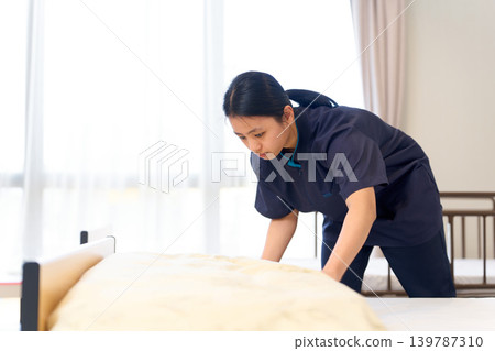 Foreign caregiver prepares bed at nursing home Foreign caregiver prepares bed at nursing home 139787310