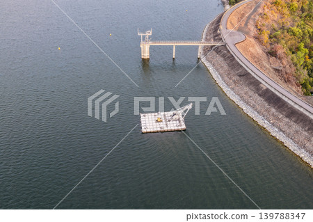 Aerial view of the Glenbawn Dam wall featuring the water intake system and servicing pontoon in NSW Australia. Drone photograph captures the engineering infrastructure, reservoir waters and Aerial view of the Glenbawn Dam wall featuring the water intake system and servicing pontoon in NSW Australia. Drone photograph captures the engineering infrastructure, reservoir waters and 139788347