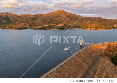 Aerial view of the Glenbawn Dam wall featuring the water intake system and servicing pontoon in NSW Australia. Drone photograph captures the engineering infrastructure, reservoir waters and Aerial view of the Glenbawn Dam wall featuring the water intake system and servicing pontoon in NSW Australia. Drone photograph captures the engineering infrastructure, reservoir waters and 139788349