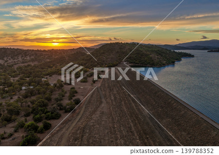 Aerial view of the Glenbawn Dam wall leading towards a sunset over the surrounding mountain range in NSW Australia. Drone photograph captures the engineering structure, expansive reservoir and Aerial view of the Glenbawn Dam wall leading towards a sunset over the surrounding mountain range in NSW Australia. Drone photograph captures the engineering structure, expansive reservoir and 139788352