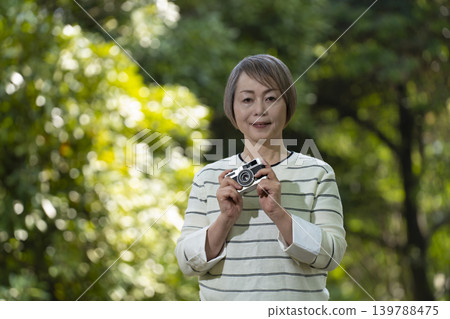 A senior woman takes photos with her camera in a park surrounded by fresh greenery. A senior woman takes photos with her camera in a park surrounded by fresh greenery. 139788475