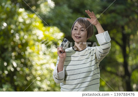 A senior woman takes photos with her camera in a park surrounded by fresh greenery. A senior woman takes photos with her camera in a park surrounded by fresh greenery. 139788476