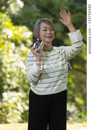 一位老婦人在綠樹環繞的公園裡用相機拍照。 一位老婦人在綠樹環繞的公園裡用相機拍照。 139788486