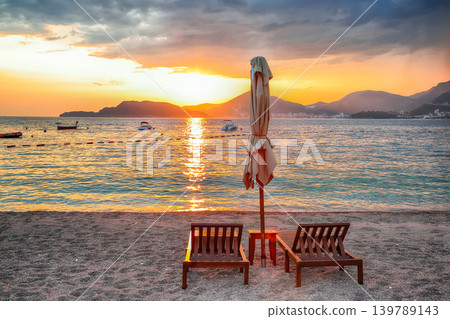 Amazing sunset at beach with chaise lounges and umbrellas in Sveti Stefan near Budva. 139789143
