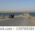 An old truck driving on a road through a lake in the middle of the desert. 139789284
