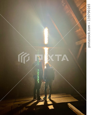 Two individuals standing in an attic illuminated by sunlight streaming through a Two individuals standing in an attic illuminated by sunlight streaming through a 139790165
