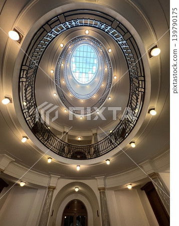 Circular architectural design featuring an ornate staircase with a glass skylight, illuminated Circular architectural design featuring an ornate staircase with a glass skylight, illuminated 139790175