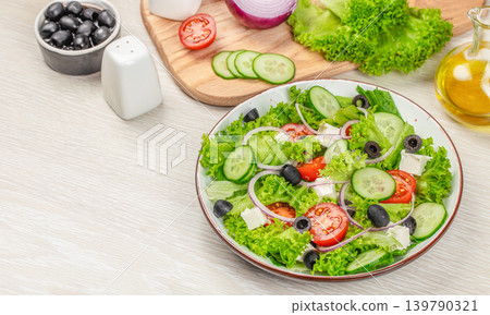 Greek salad with lettuce cucumber olives and feta cheese on light wooden background Greek salad with lettuce cucumber olives and feta cheese on light wooden background 139790321