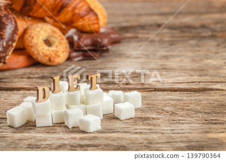 Diet concept with sugar cubes and unhealthy sweet food on wooden background with copy space Diet concept with sugar cubes and unhealthy sweet food on wooden background with copy space 139790364