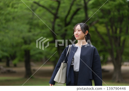 A businesswoman gazes straight ahead against a backdrop of lush green trees. A businesswoman gazes straight ahead against a backdrop of lush green trees. 139790446