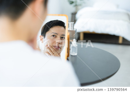 Beauty image: A man doing skincare while looking in a mirror. Beauty image: A man doing skincare while looking in a mirror. 139790564