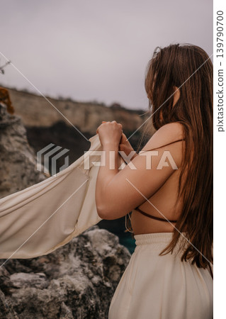 Woman cliff ocean standing on a rocky shore while holding a cream colored jacket under a moody overcast sky 139790700