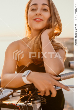 Woman bicycle sunset smiling young woman leaning on her bicycle at the coast during golden hour for a relaxed lifestyle concept Woman bicycle sunset smiling young woman leaning on her bicycle at the coast during golden hour for a relaxed lifestyle concept 139790756