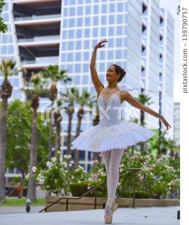 Ballerina dancing on pointe in urban plaza with modern city skyline Ballerina dancing on pointe in urban plaza with modern city skyline 139790757