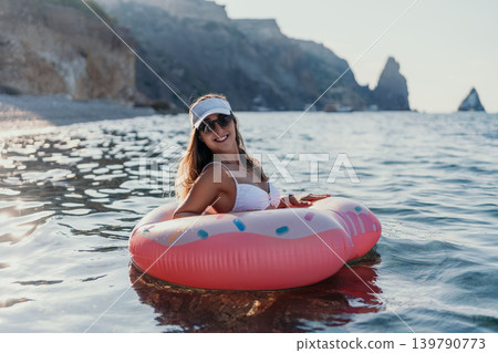 Woman, ocean, donut. Relaxing woman floats in ocean with donut ring near coastal cliffs, summer vacation. Woman, ocean, donut. Relaxing woman floats in ocean with donut ring near coastal cliffs, summer vacation. 139790773