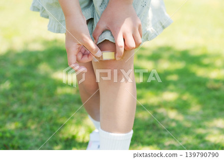 Elementary school student putting a bandage on his knee Elementary school student putting a bandage on his knee 139790790