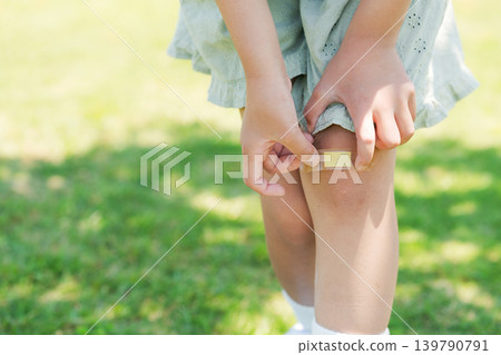 一名小學生正在為自己的膝蓋貼繃帶 一名小學生正在為自己的膝蓋貼繃帶 139790791