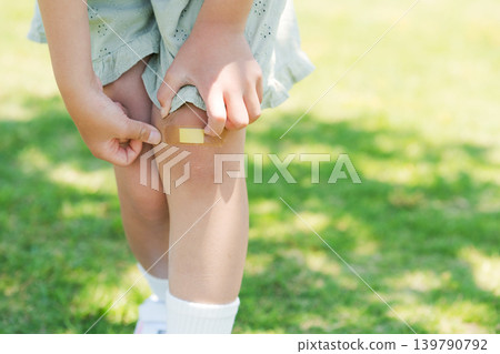 Elementary school student putting a bandage on his knee Elementary school student putting a bandage on his knee 139790792