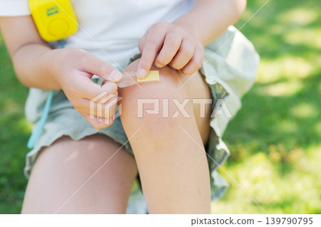 一名小學生正在為自己的膝蓋貼繃帶 一名小學生正在為自己的膝蓋貼繃帶 139790795